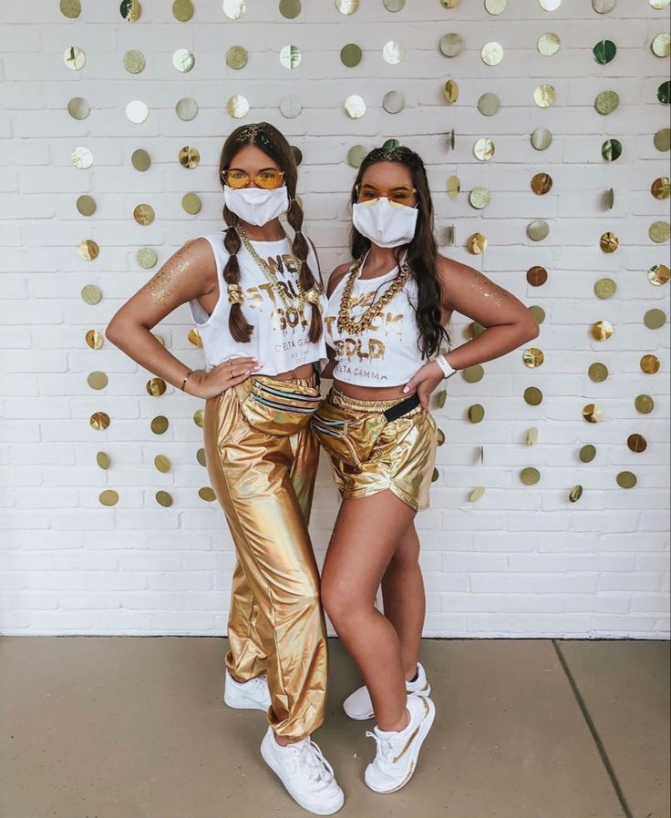 two girls in gold pants and masks posing for the camera with their hands on their hips