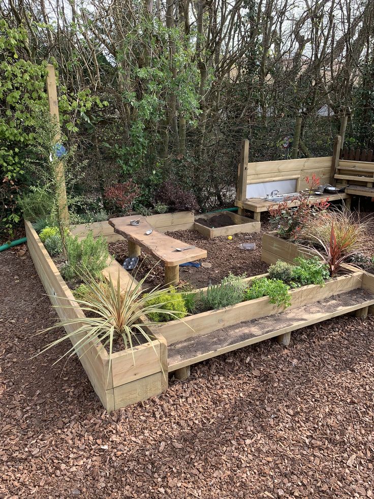 a wooden bench sitting next to a garden filled with lots of plants and flowers on top of mulch covered ground