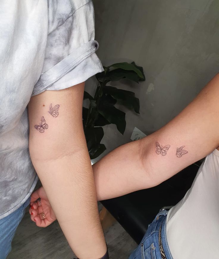 two people holding hands with tattoos on their arms and one has a butterfly tattoo on the arm