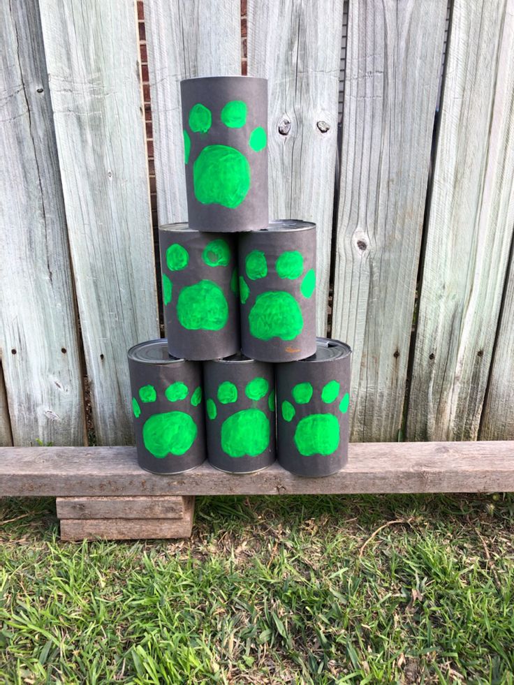 four green paw prints on black toilet paper rolls sitting in front of a wooden fence