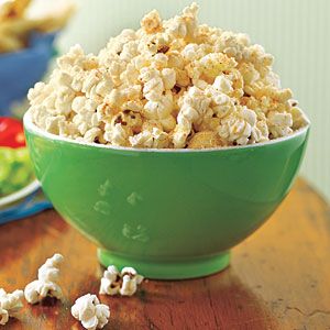 a green bowl filled with popcorn on top of a wooden table