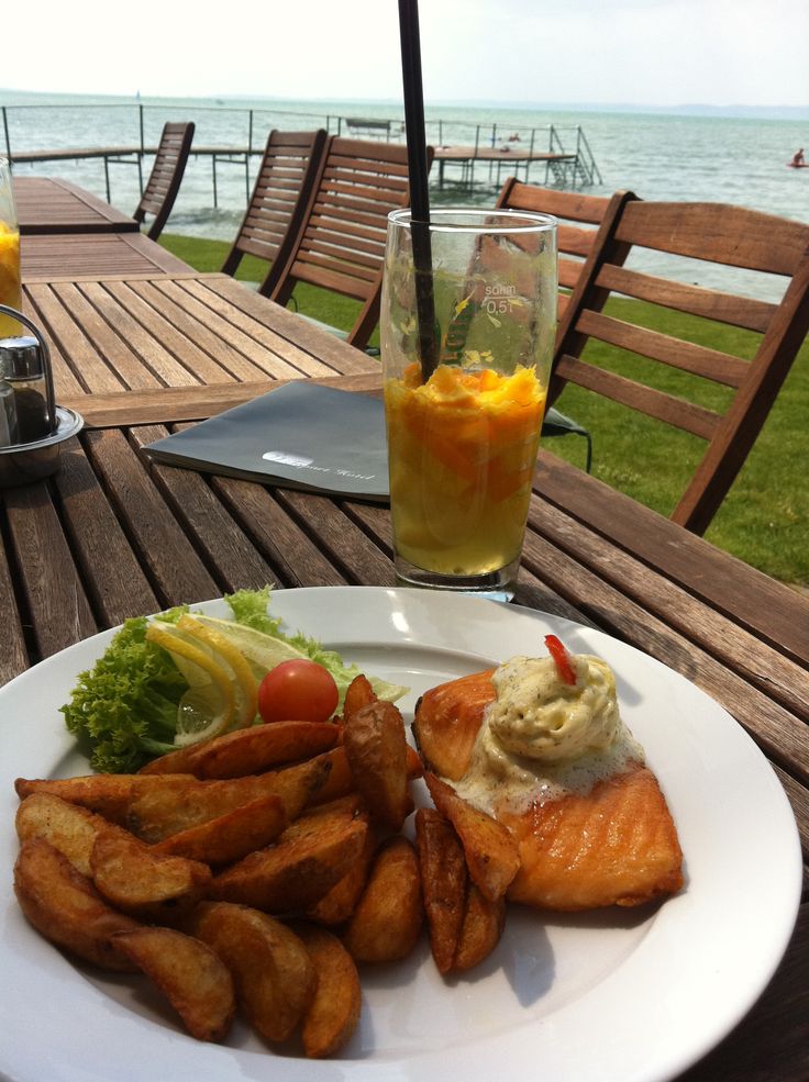 a white plate topped with fish and fries next to a glass of orange juice on top of a wooden table