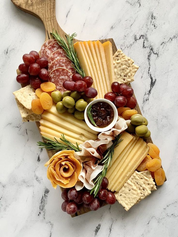 cheese, crackers, grapes and olives are arranged on a marble platter