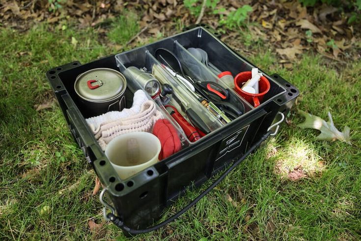 a black box filled with lots of different items on top of green grass next to trees