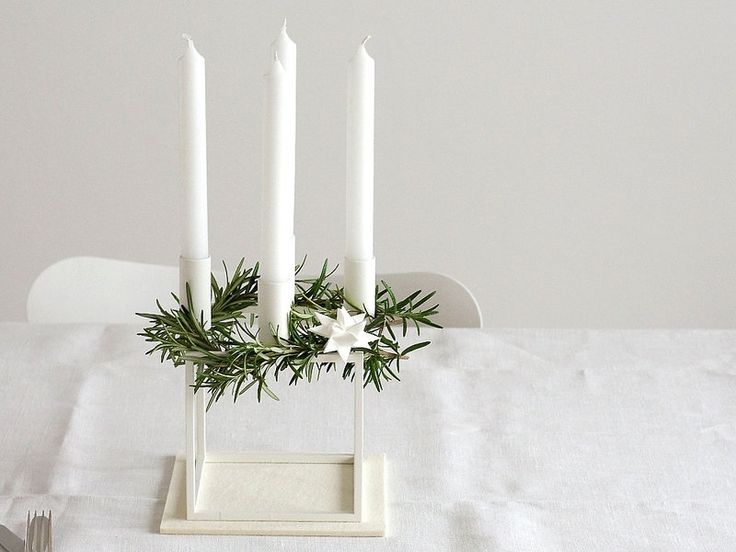 four white candles are placed on a table with greenery and silverware in the foreground