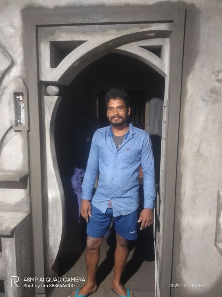 a man in blue shirt and shorts standing at the entrance to a cave like building