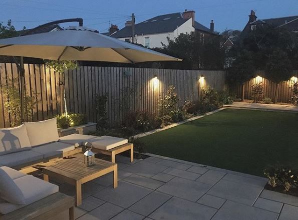 a backyard with lawn, patio furniture and an umbrella lit up in the evening time