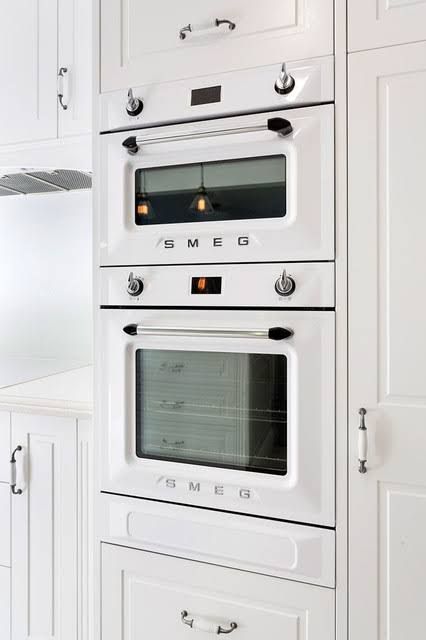 two white ovens side by side in a kitchen with white cabinets and counter tops