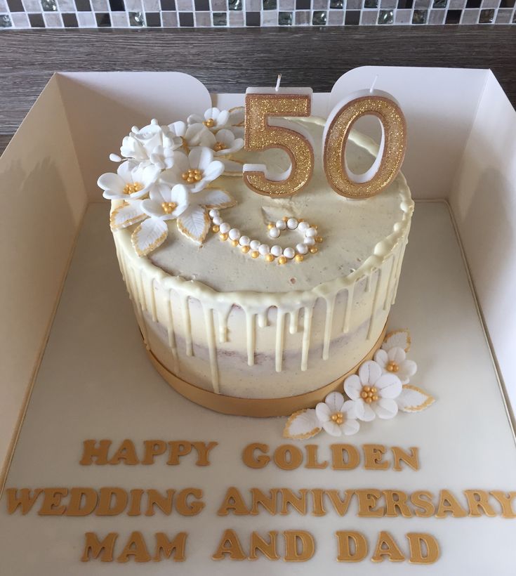 a 50th birthday cake in a box with gold lettering and flowers on the top is decorated with white icing