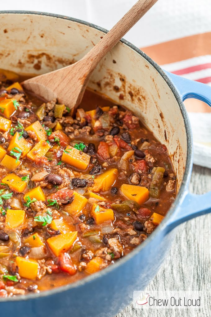 a blue pot filled with stew next to a wooden spoon on top of a table