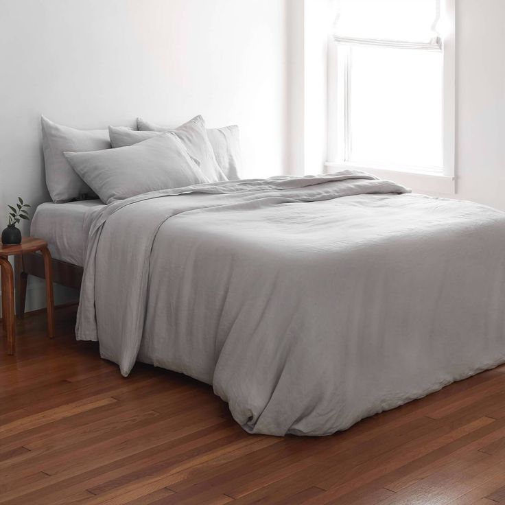 a bed sitting on top of a hard wood floor next to a window with white sheets