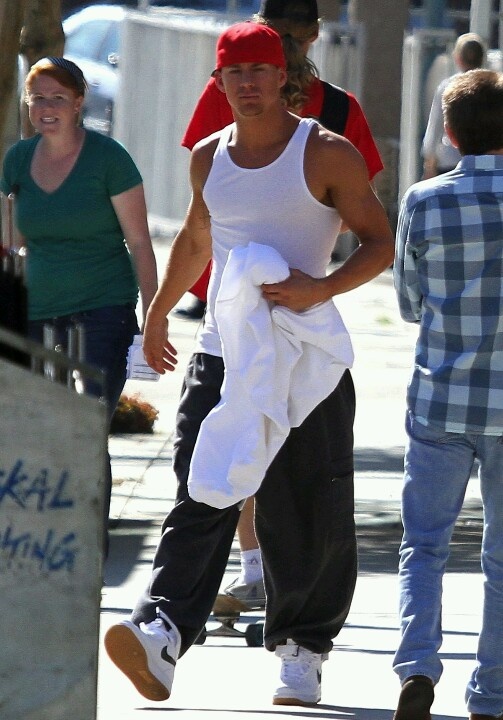 a man in white shirt and black pants walking on sidewalk with other people behind him