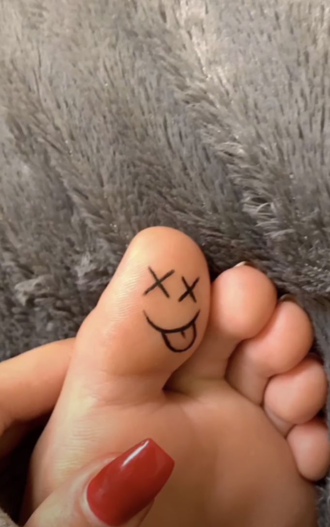 a person with a smiley face drawn on their toe and nail polishing the toes