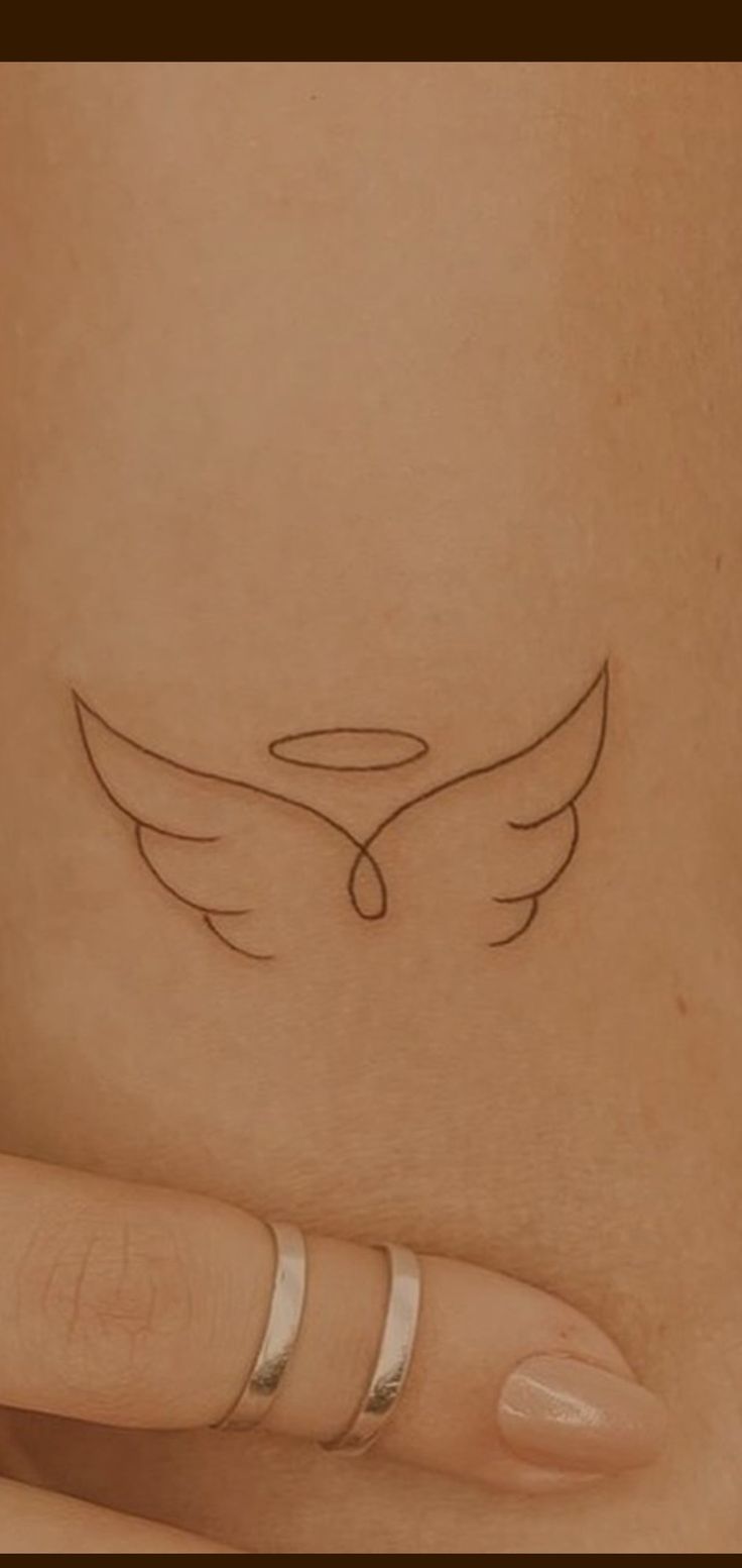 a woman's hand with a small tattoo on her left arm and an angel wing