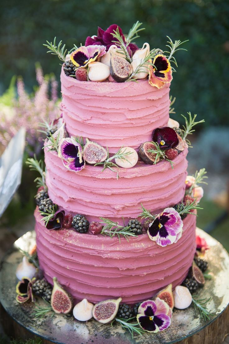 a three tiered cake with fresh flowers and fruit on top is sitting on a tree stump