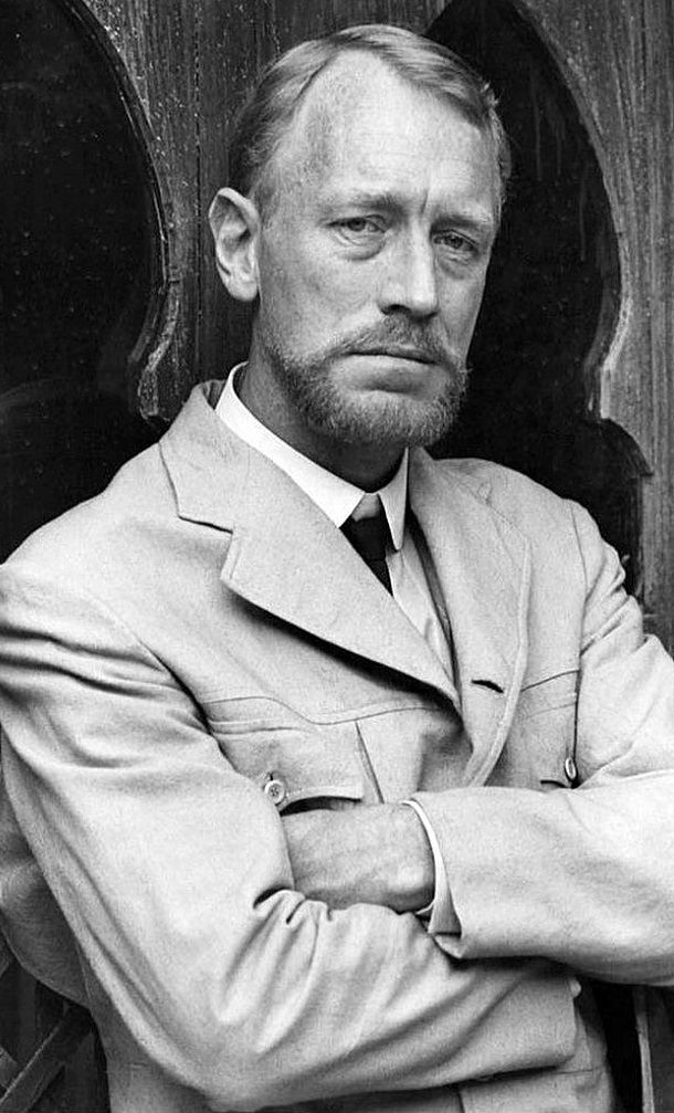 a man in a suit and tie leaning against a wooden wall with his arms crossed