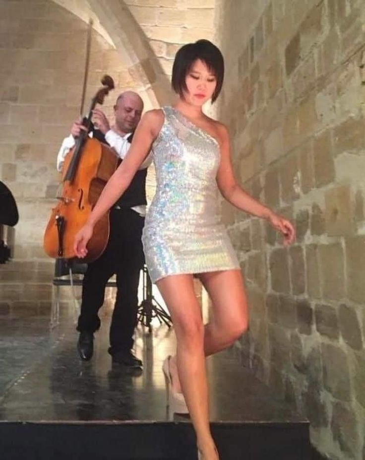 a woman in a short silver dress is walking down the stairs with an instrument behind her