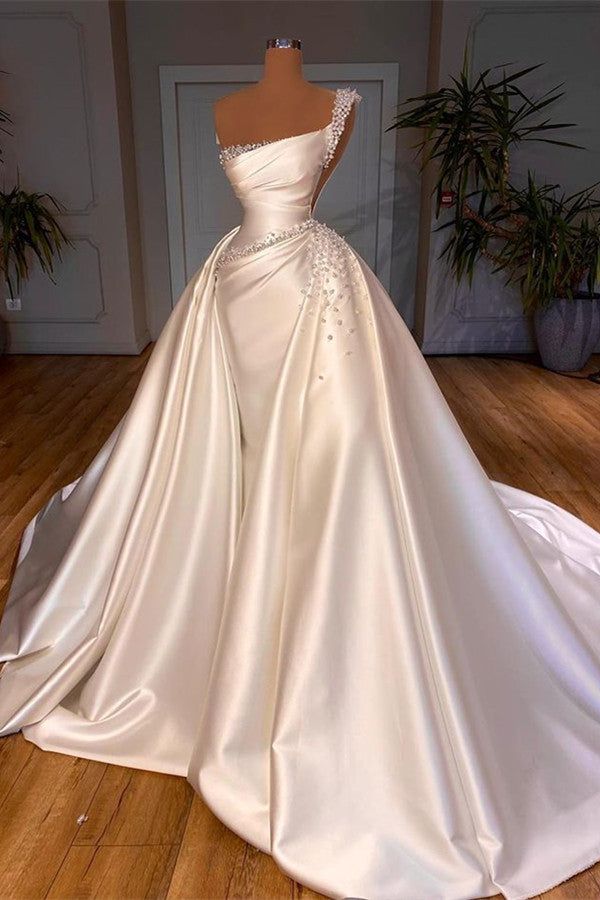 a white wedding dress on display in a room with wooden floors and potted plants