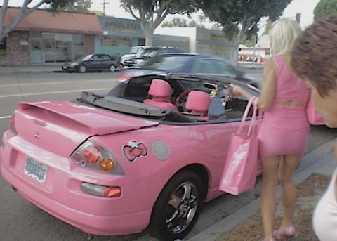 a woman in a pink dress standing next to a pink car