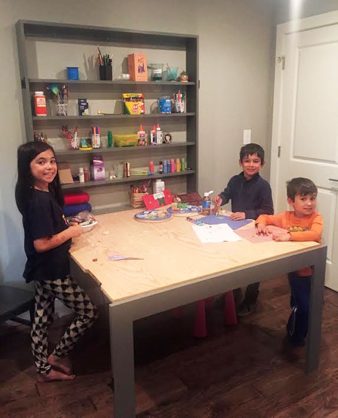 three children are sitting at a table in the middle of a room with bookshelves