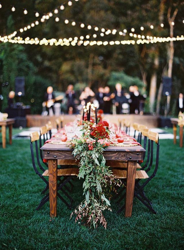 an outdoor dinner table set up with candles and greenery on the grass, surrounded by string lights