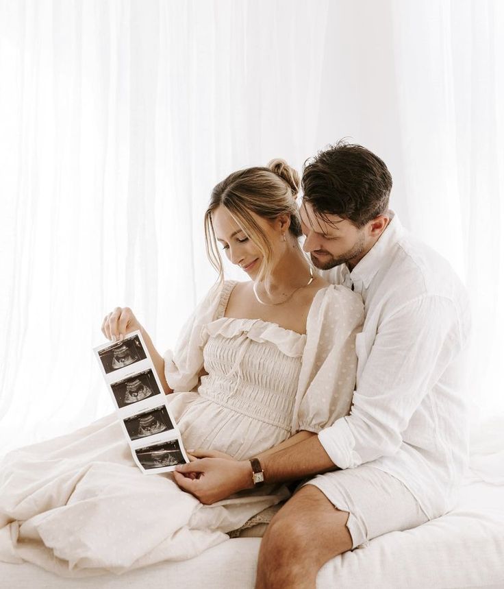 a man and woman sitting on top of a bed next to each other holding an electronic device