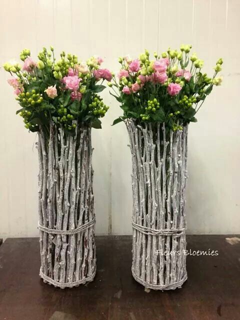 two metal vases with flowers in them on a wooden table next to each other