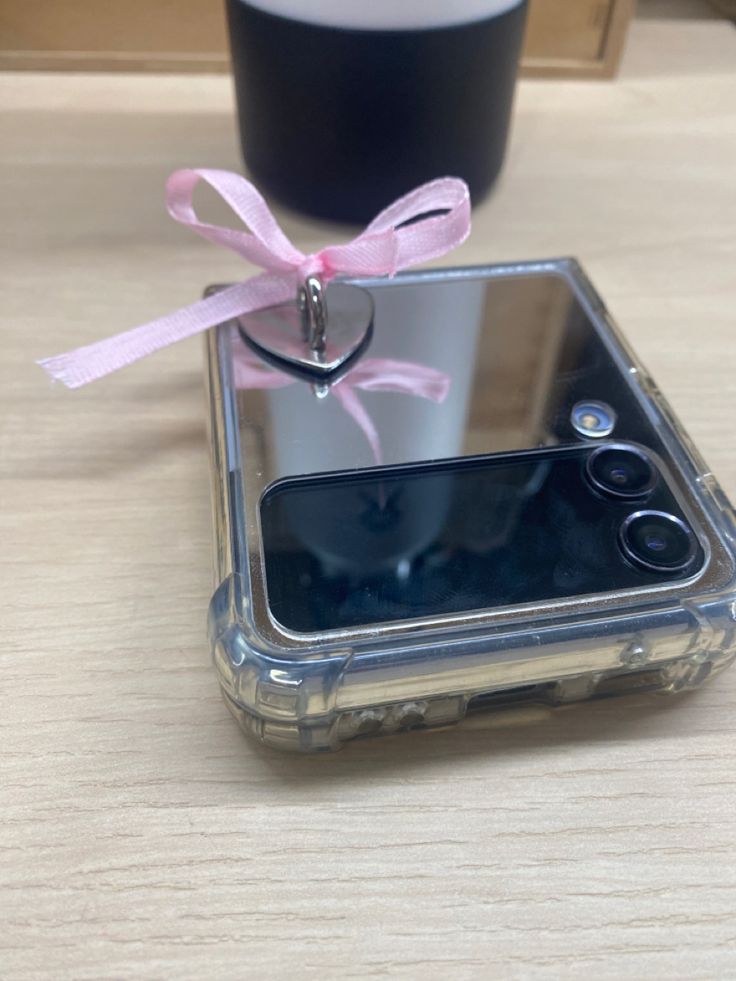 a cell phone with a pink ribbon tied to it's back sitting on a table