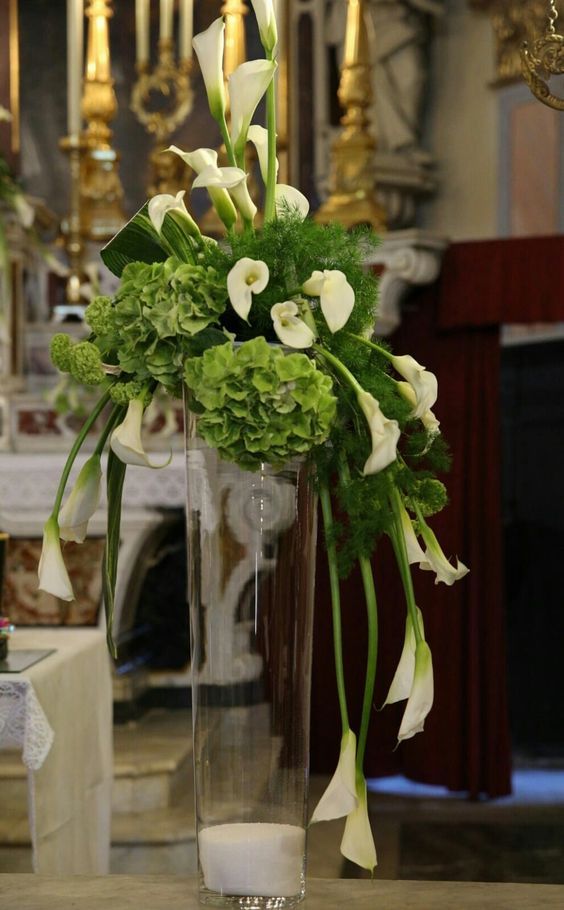 a vase filled with white flowers and greenery on top of a table next to a chandelier