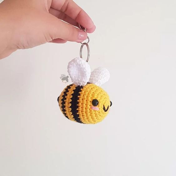 a hand holding a crocheted key chain with a bee on it