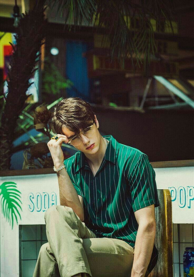 a young man sitting on top of a wooden chair next to a palm tree in front of a store