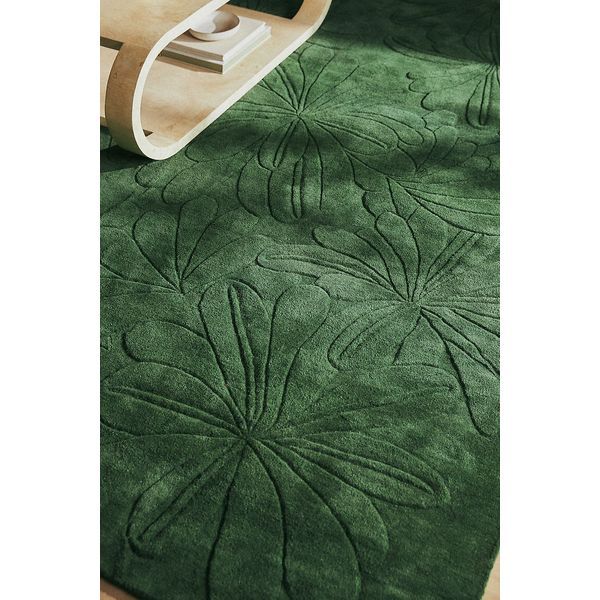 a green rug with an intricate design on the bottom, and a white chair in the background