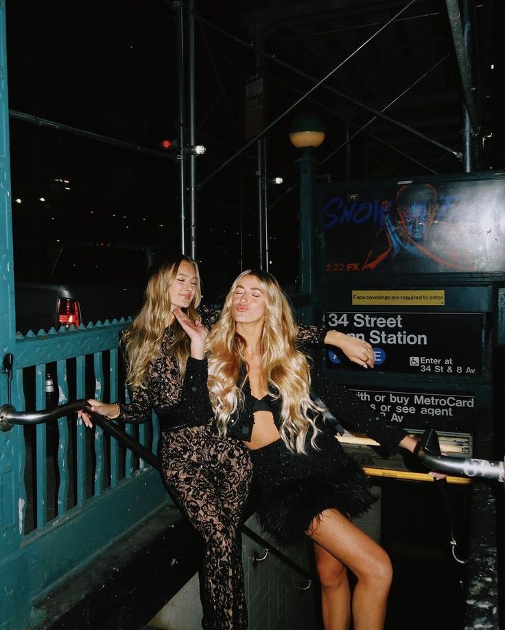 two beautiful young women sitting next to each other in front of a sign at night