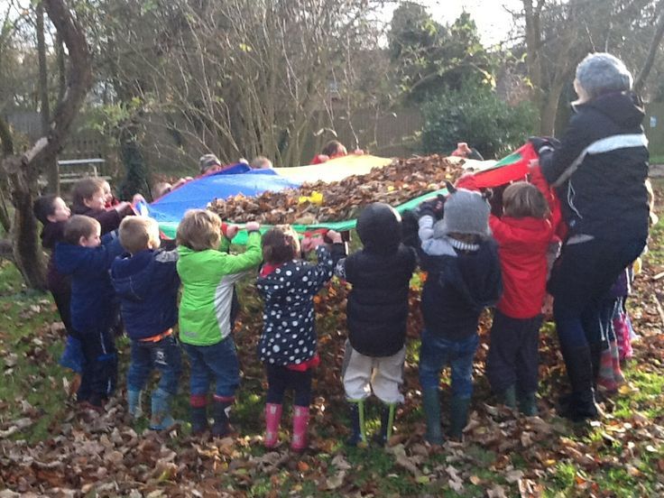 a group of children standing in front of a colorful kite on top of leaf covered ground