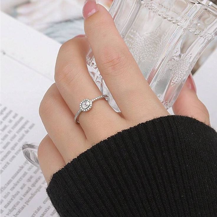 a woman's hand holding a clear glass bottle with a diamond ring on it