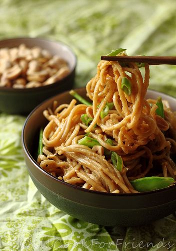 two bowls filled with noodles and vegetables on top of a green cloth covered tablecloth