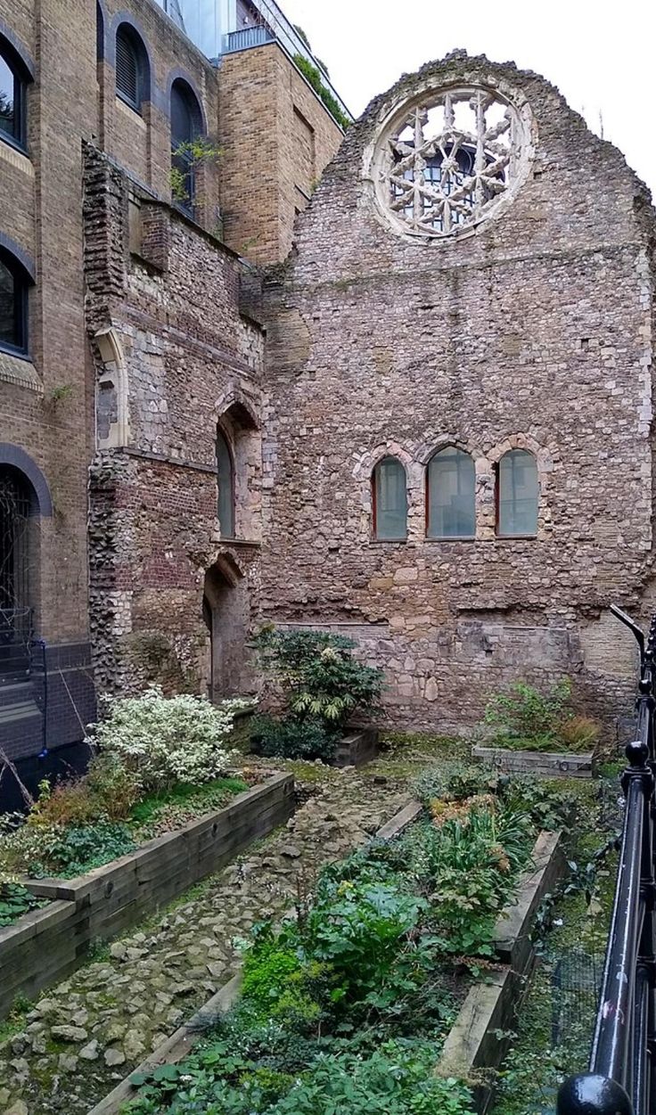 an old brick building with many windows and plants growing in the garden area next to it