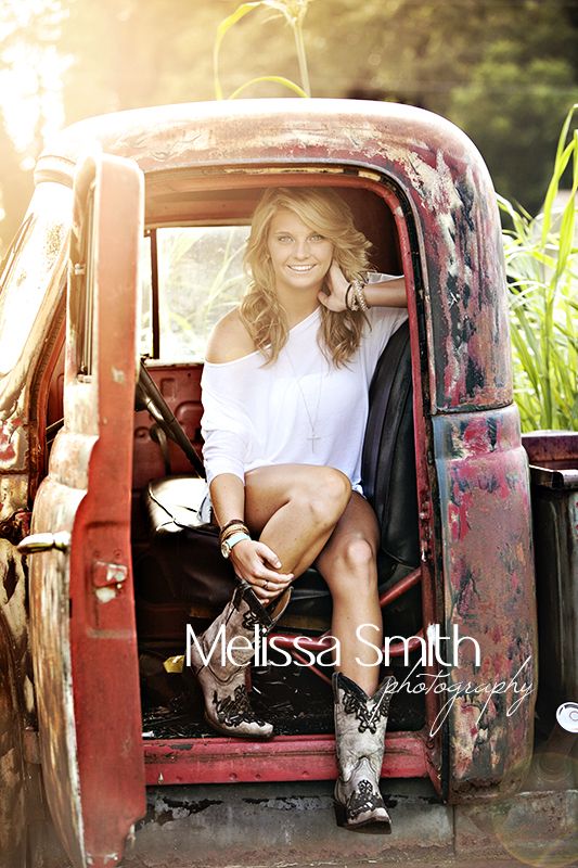 a woman sitting in the back of an old red truck with her legs crossed and boots on