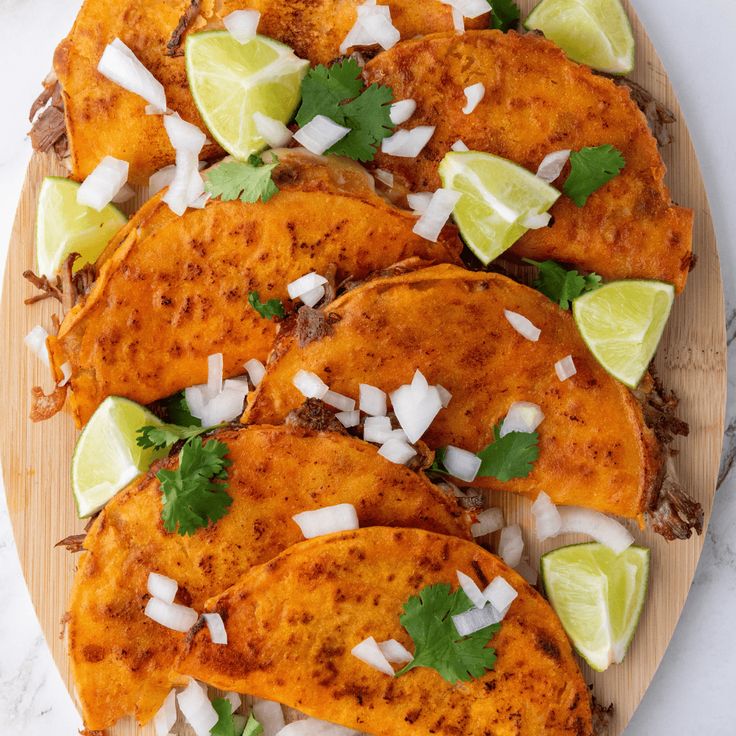 some tacos are on a wooden plate with limes and cilantro wedges