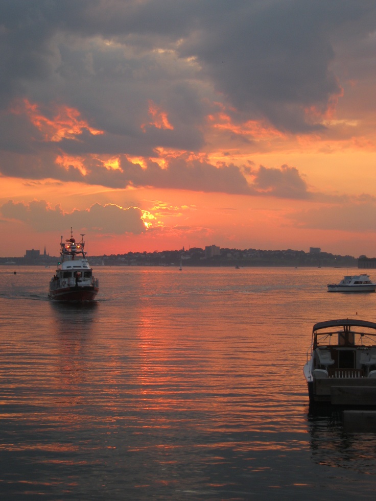 two boats floating on top of a large body of water under a cloudy sky at sunset