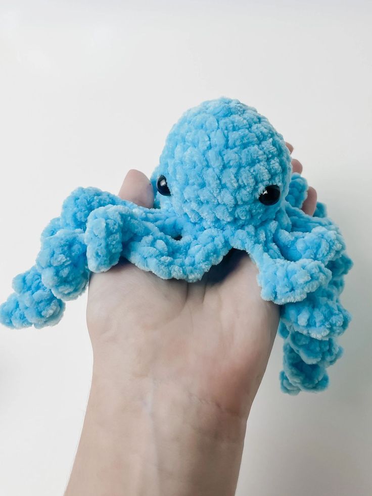 a hand holding a small blue crocheted octopus