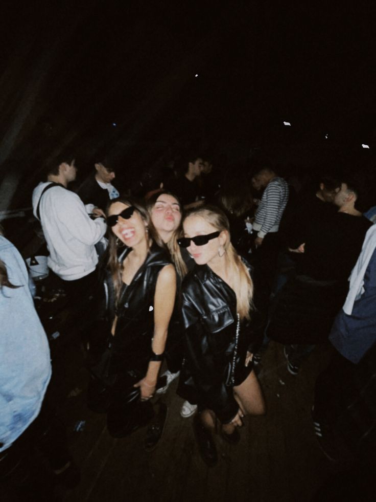 three women in leather jackets are posing for the camera at a party with other people