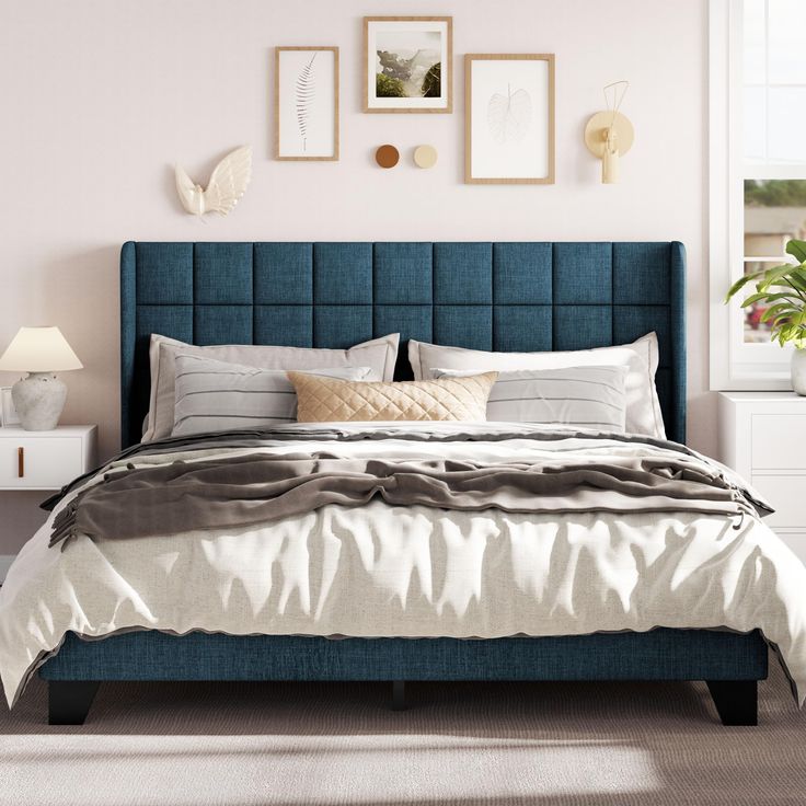 a bed with blue headboard and pillows in a white room next to pictures on the wall