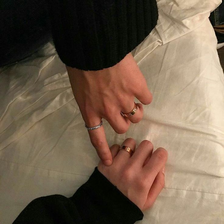 two people holding hands on top of a white bed with their fingers touching each other