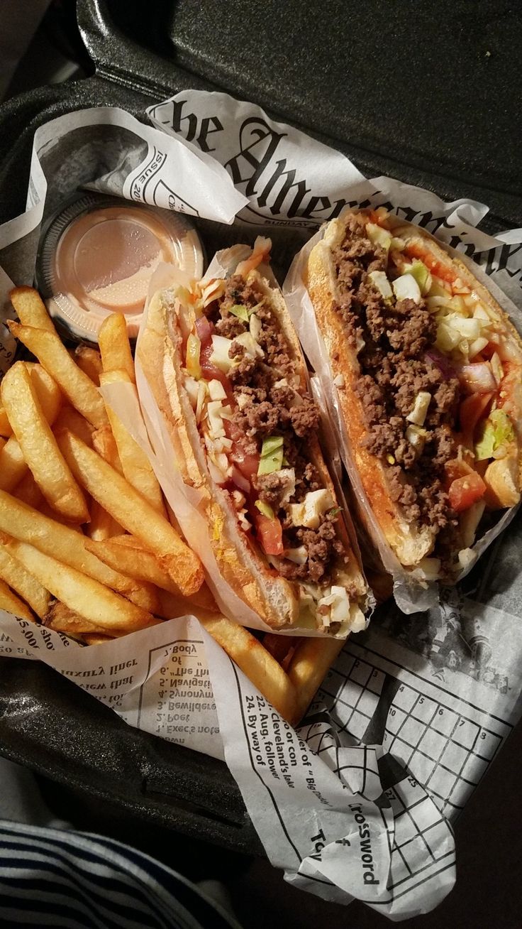 two sandwiches and french fries on a tray with paper wrappers next to each other