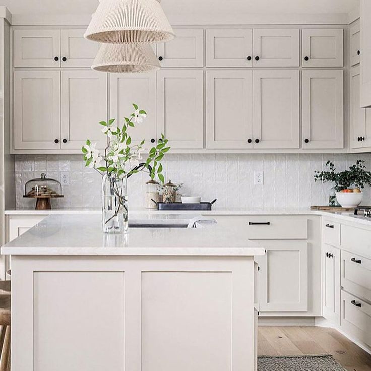 a kitchen with white cabinets and an island in the middle is decorated with greenery