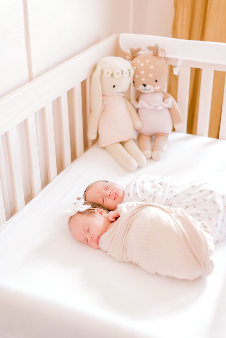 a baby sleeping in a white crib with stuffed animals behind it on the bed