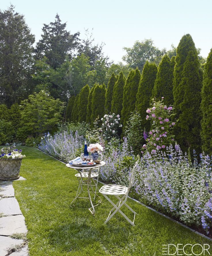 a garden with lots of flowers and plants on the grass, along with a table and chairs