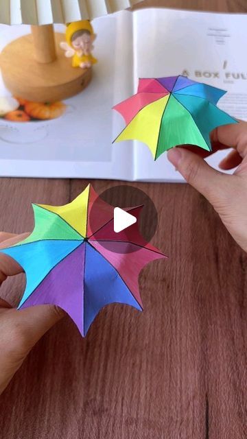 someone is holding an origami umbrella over a book on a wooden table,