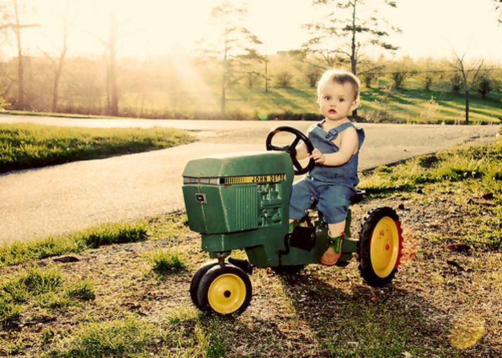 a young boy riding on the back of a green tractor